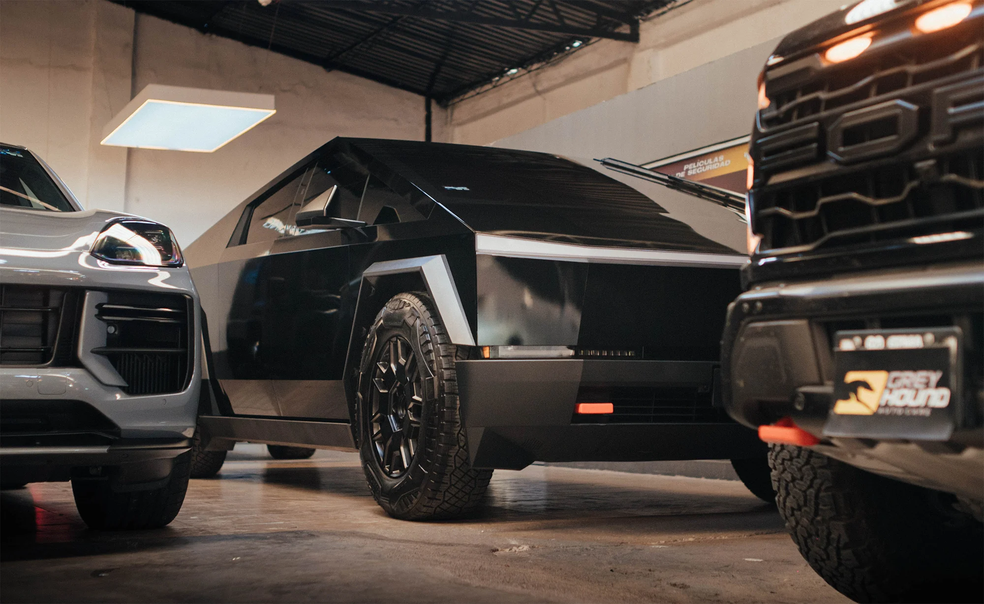 Tesla Cybertruck junto a Porsche Cayenne y Ford Raptor dentro del taller de Grey Hound Auto Care